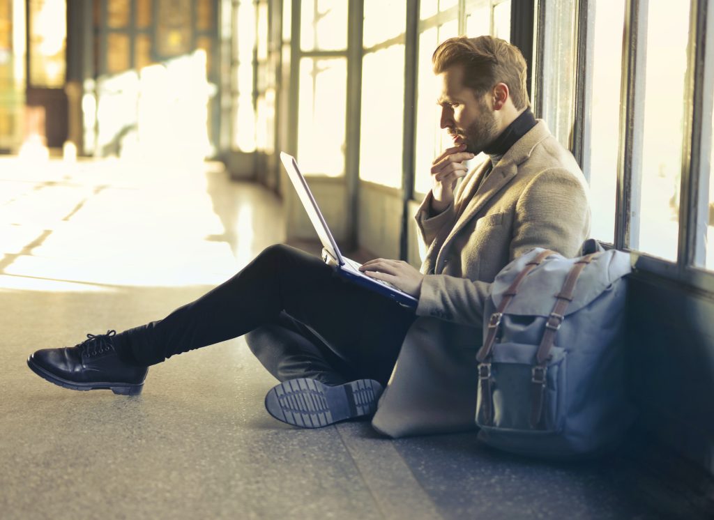 A person sitting on the floor with a laptop and backpack.